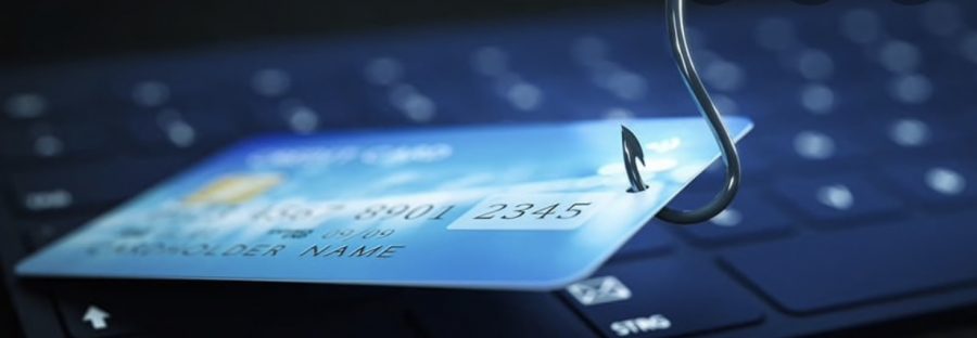 A fishing hook pierces a credit card on a keyboard, symbolizing financial phishing scams.