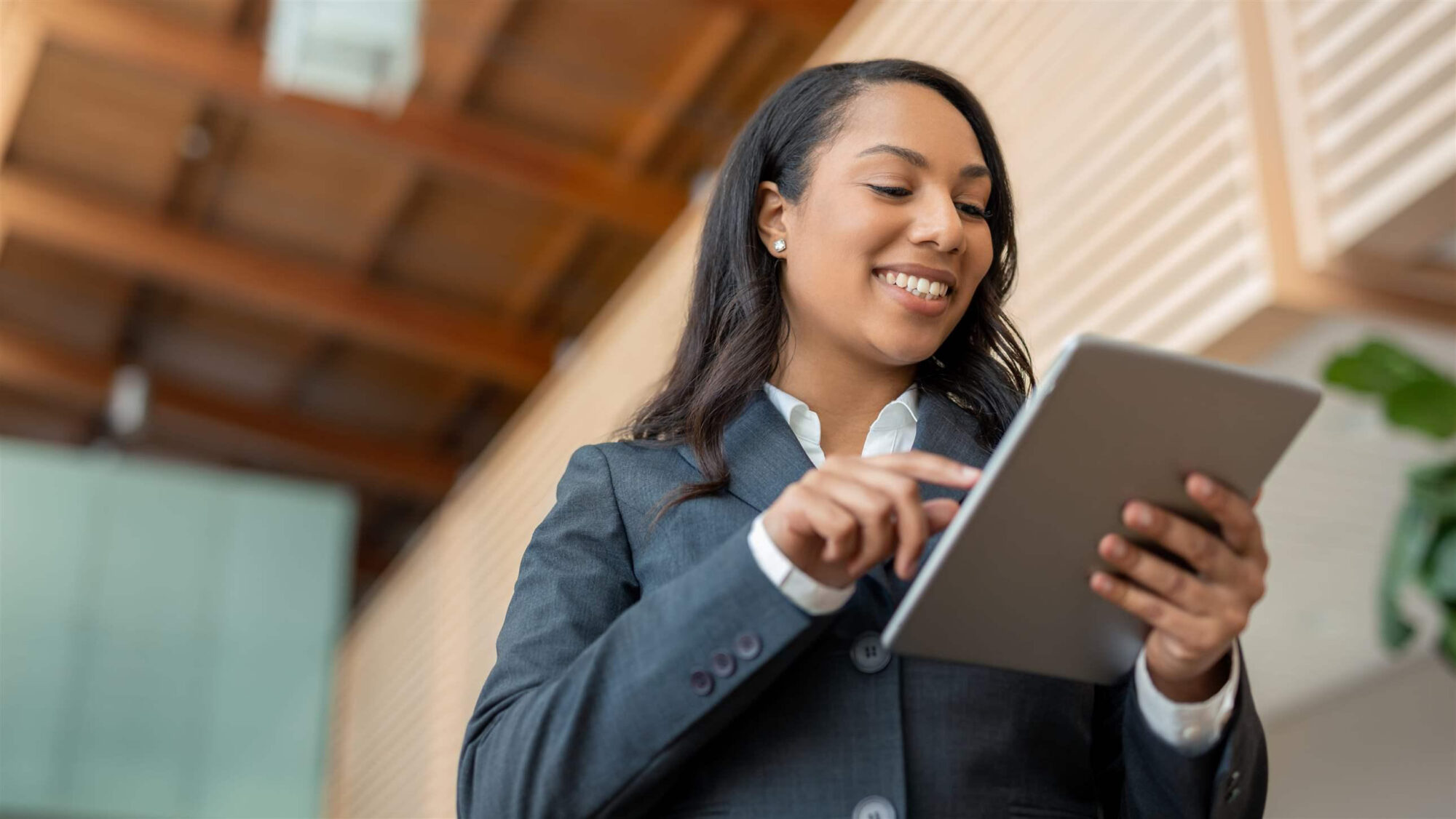 A smiling woman in business attire interacts with a tablet