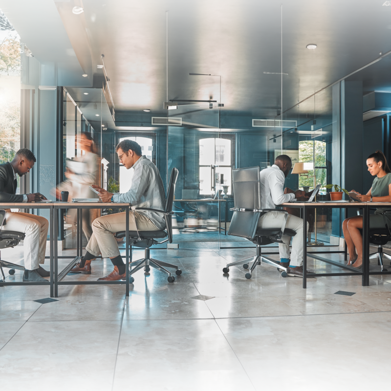 A diverse group of professionals works diligently in a modern, glass-walled office environment.