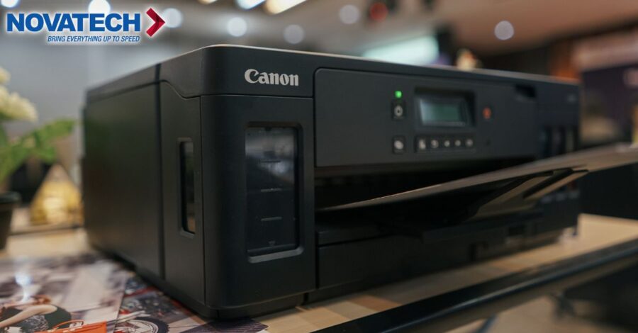 A black Canon printer with the Novatech logo is displayed on a table with papers.