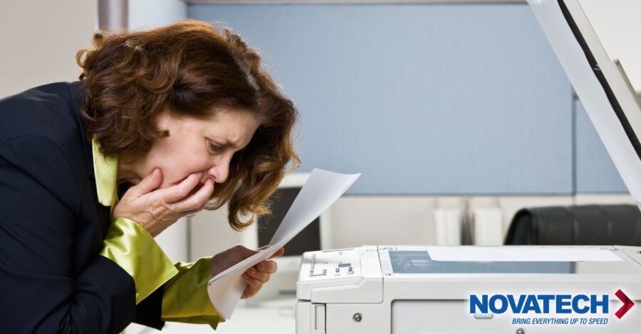 A distressed woman holds a document near a copier, her hands covering her mouth in dismay.